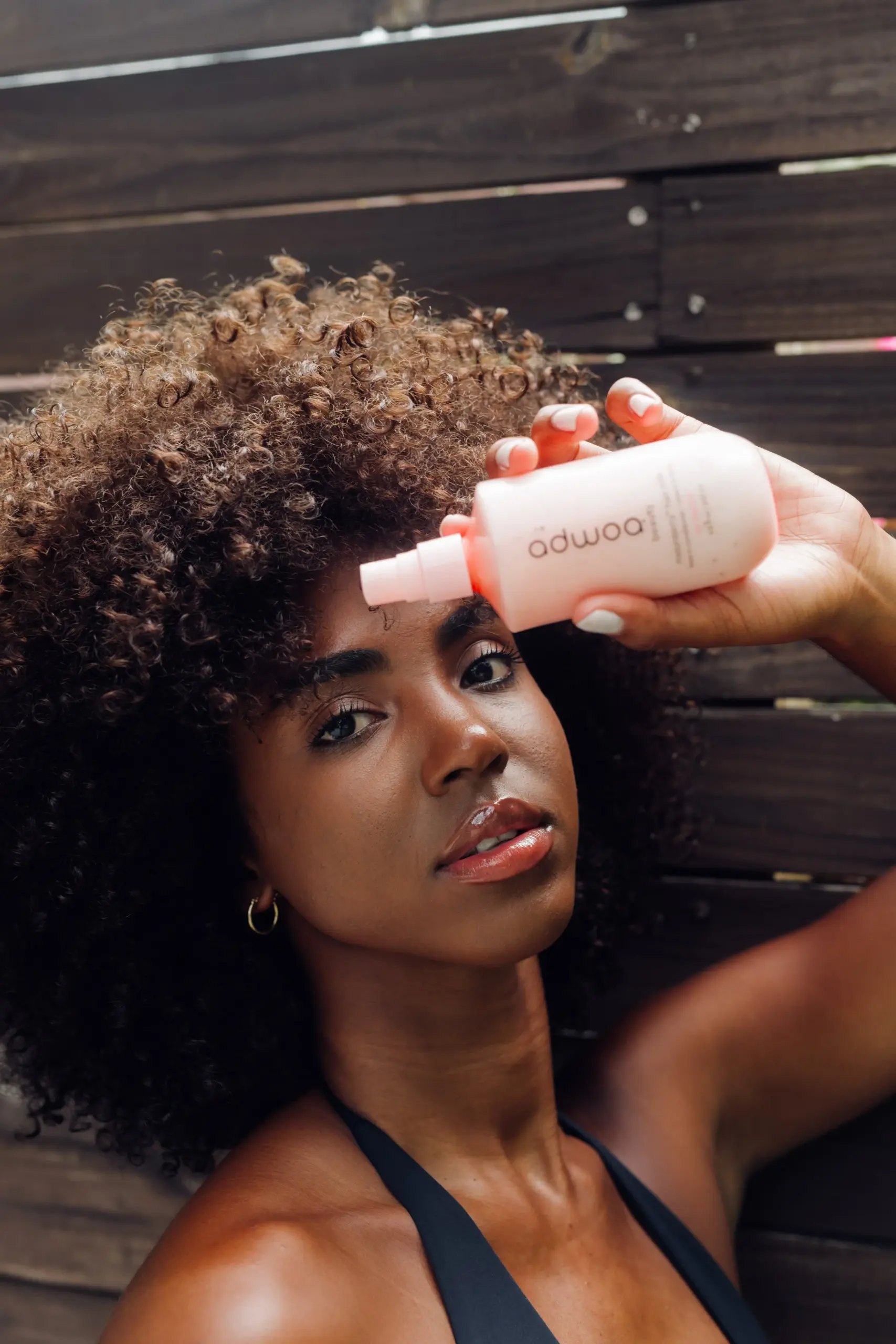Black woman with Type 4A natural hair applying Adwoa Beauty Baomint Moisturizing Leave-in Conditioner to a sectioned strand