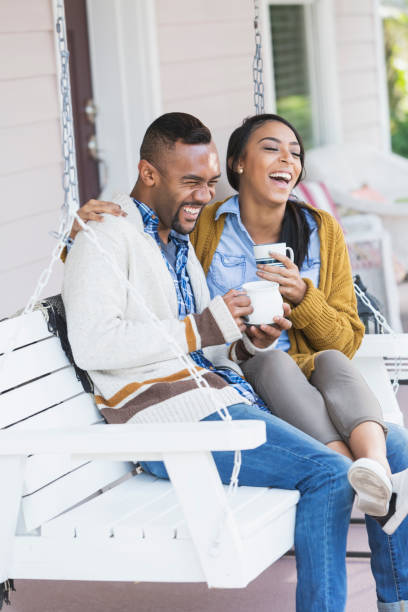 Couple laughing together on a porch swing with coffee in the morning light