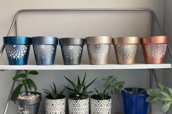Hand-painted terracotta pots in modern colors arranged on a shelf