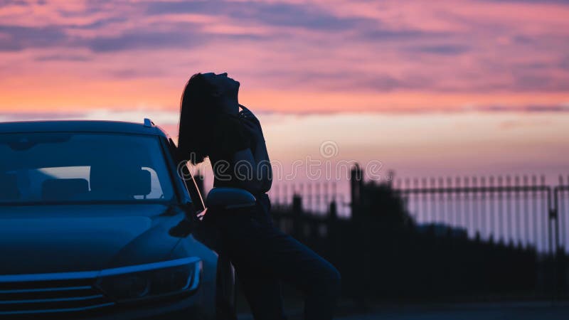Plus-size woman at a scenic road trip stop leaning against a car at sunset