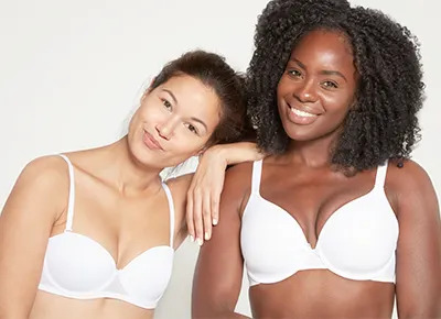 Plus-size woman being fitted for a bra in front of a mirror with a soft measuring tape, editorial fit-guide reference