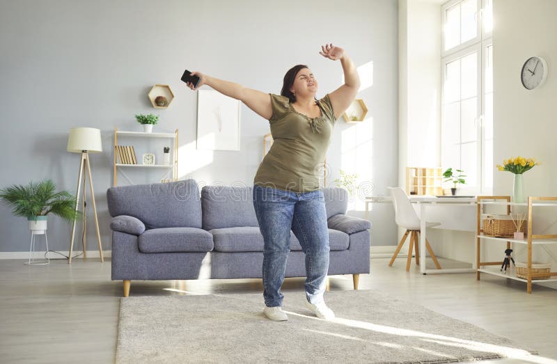 Plus-size woman dancing joyfully in her living room with wireless earbuds and a big smile