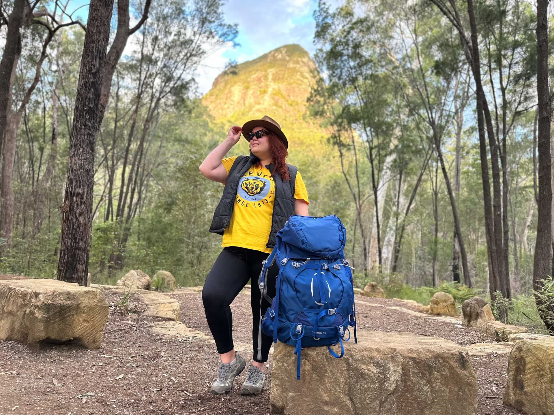 Plus-size woman hiking on a sunlit forest trail with daypack looking peaceful and strong