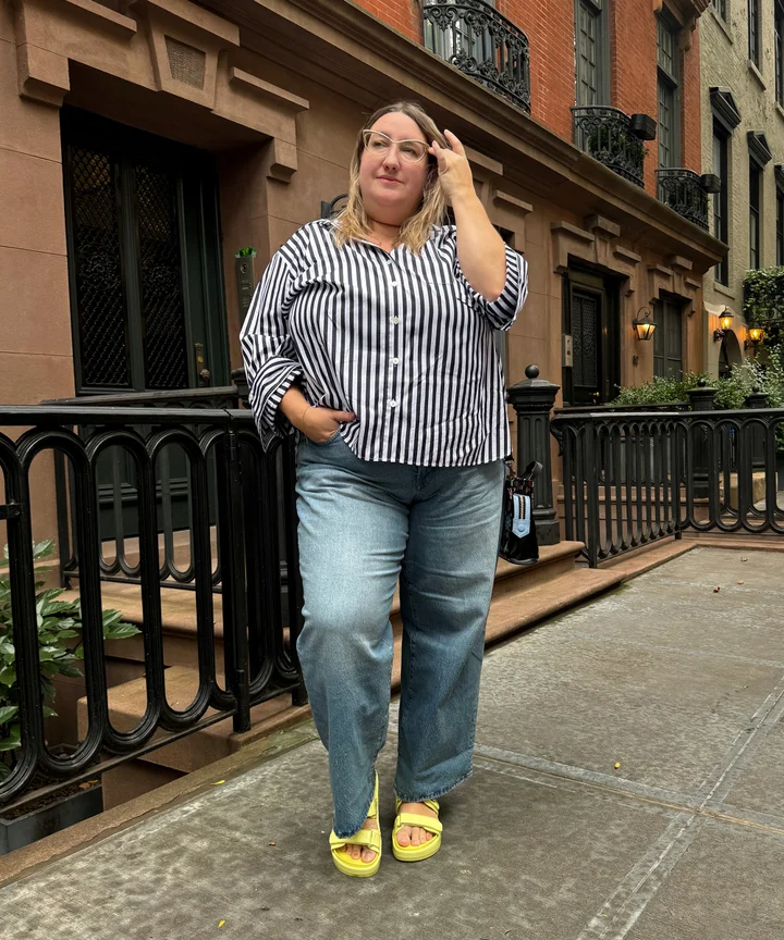 Plus-size woman styled in dark indigo baggy jeans with a fitted tucked tank and loafers, editorial street style