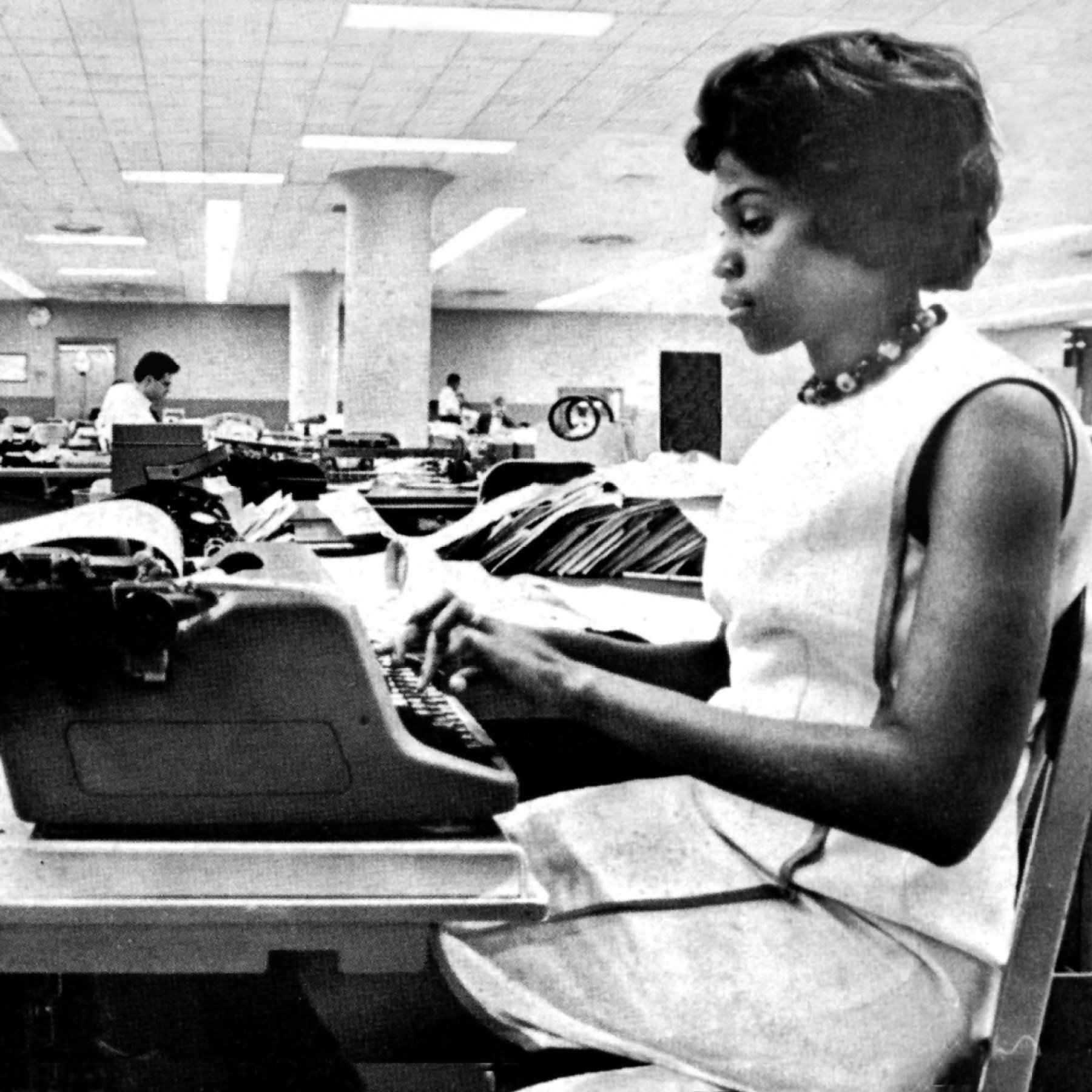 Black woman traveler at a federal passport agency window handing documents across to a uniformed clerk