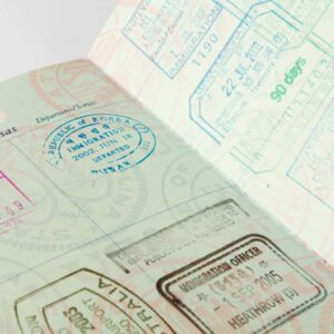 A US passport open to a page of multiple country entry stamps next to a visa application and a printed flight itinerary on a wood desk