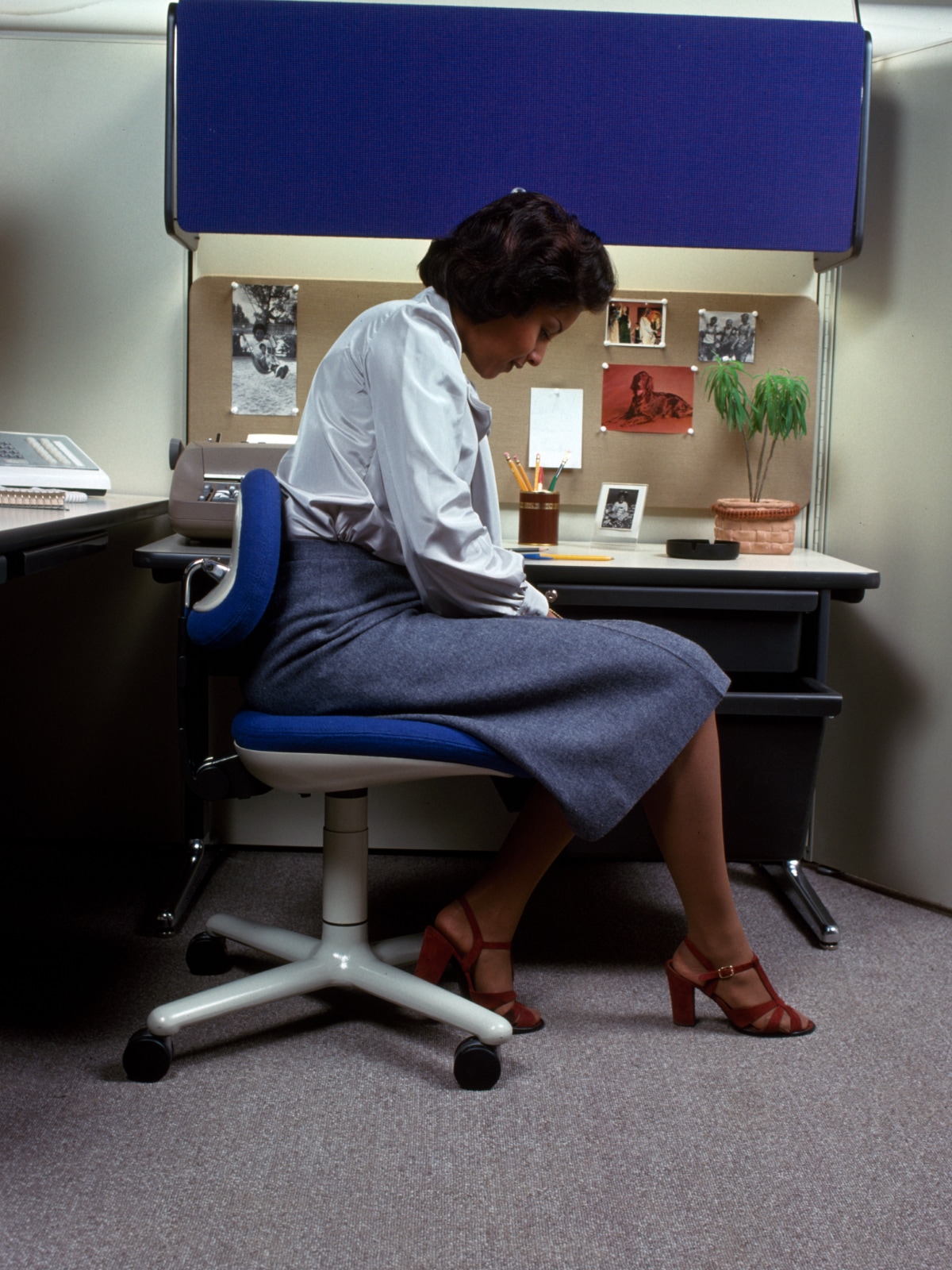Plus-size Black woman in business casual seated at a Decatur tech-company desk during an annual ergonomics evaluation with a Herman Miller Aeron chair visible behind her in morning light