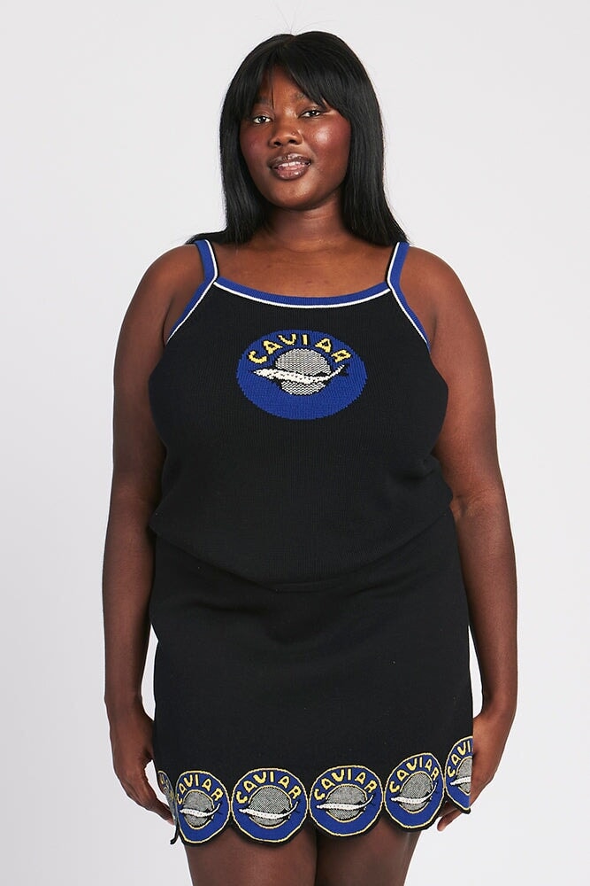A plus-size Black woman in a Brooklyn closet at golden hour setting up five outfits on a garment rod with day-of-week tags pinned to each hanger and a Yamazaki valet stand in the foreground