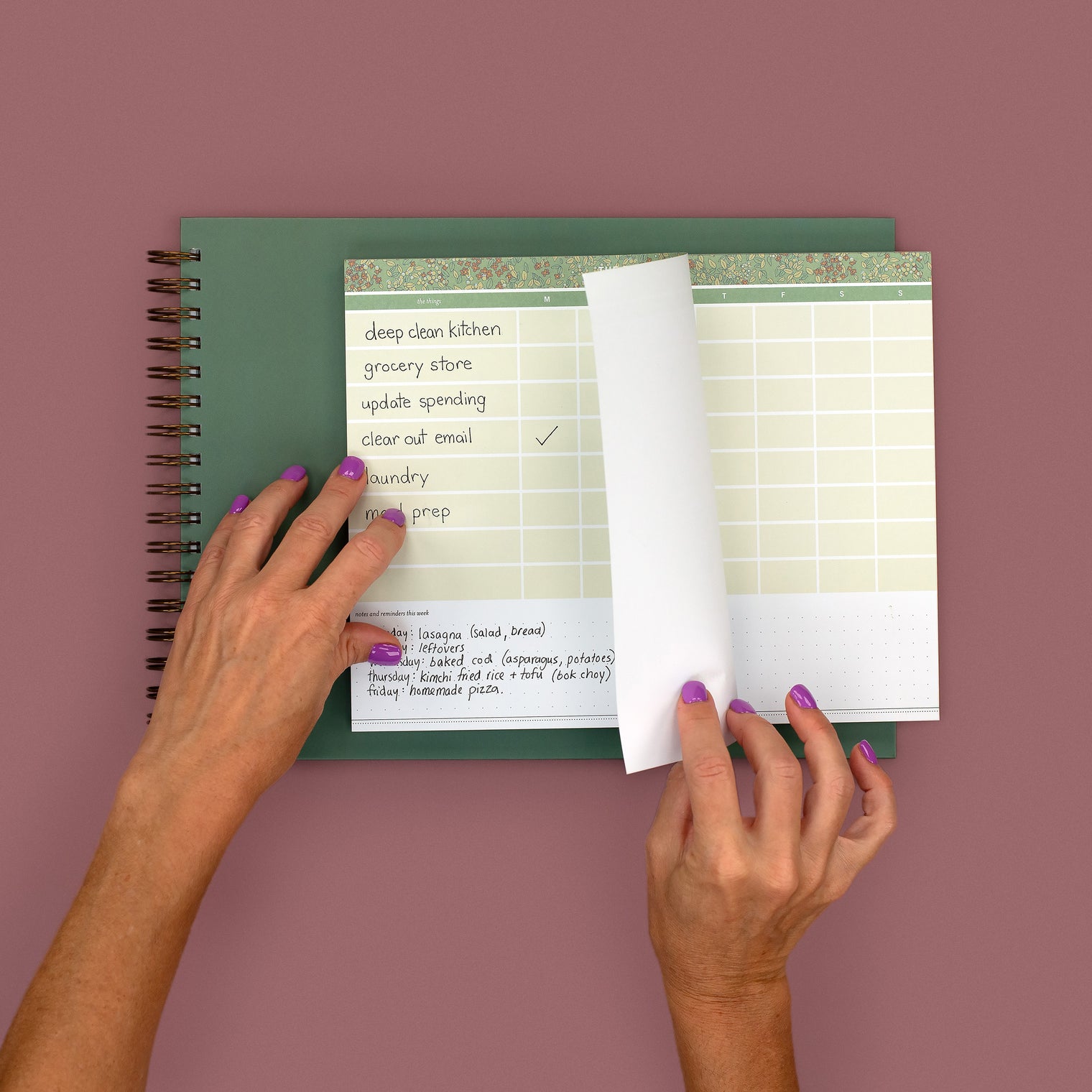 Hands holding a small notebook with a 5-column Monday-to-Friday grid of handwritten outfit notes and a phone showing a stopwatch at 6 minutes 12 seconds during the Sunday closet rewind phase