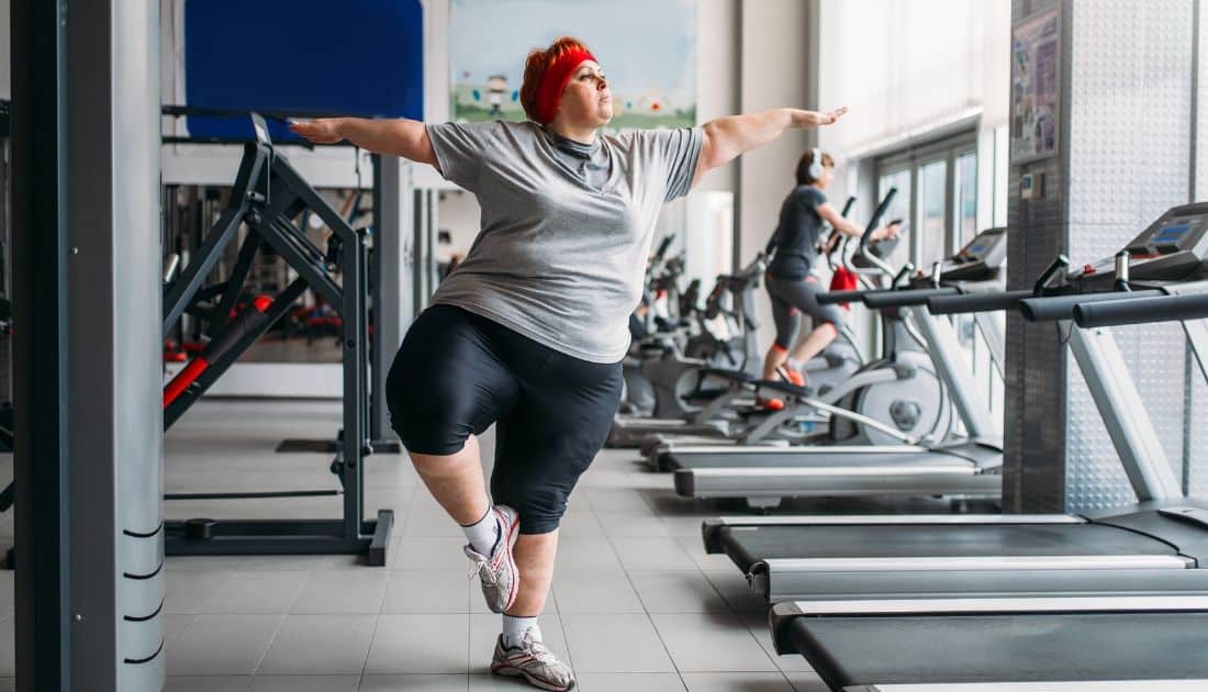 A plus-size pregnant woman walking on a treadmill in a community gym, water bottle on the console