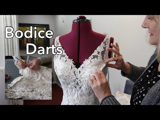 Close-up of a seamstress's hands pinning the bust seam of a satin wedding gown on a dress form