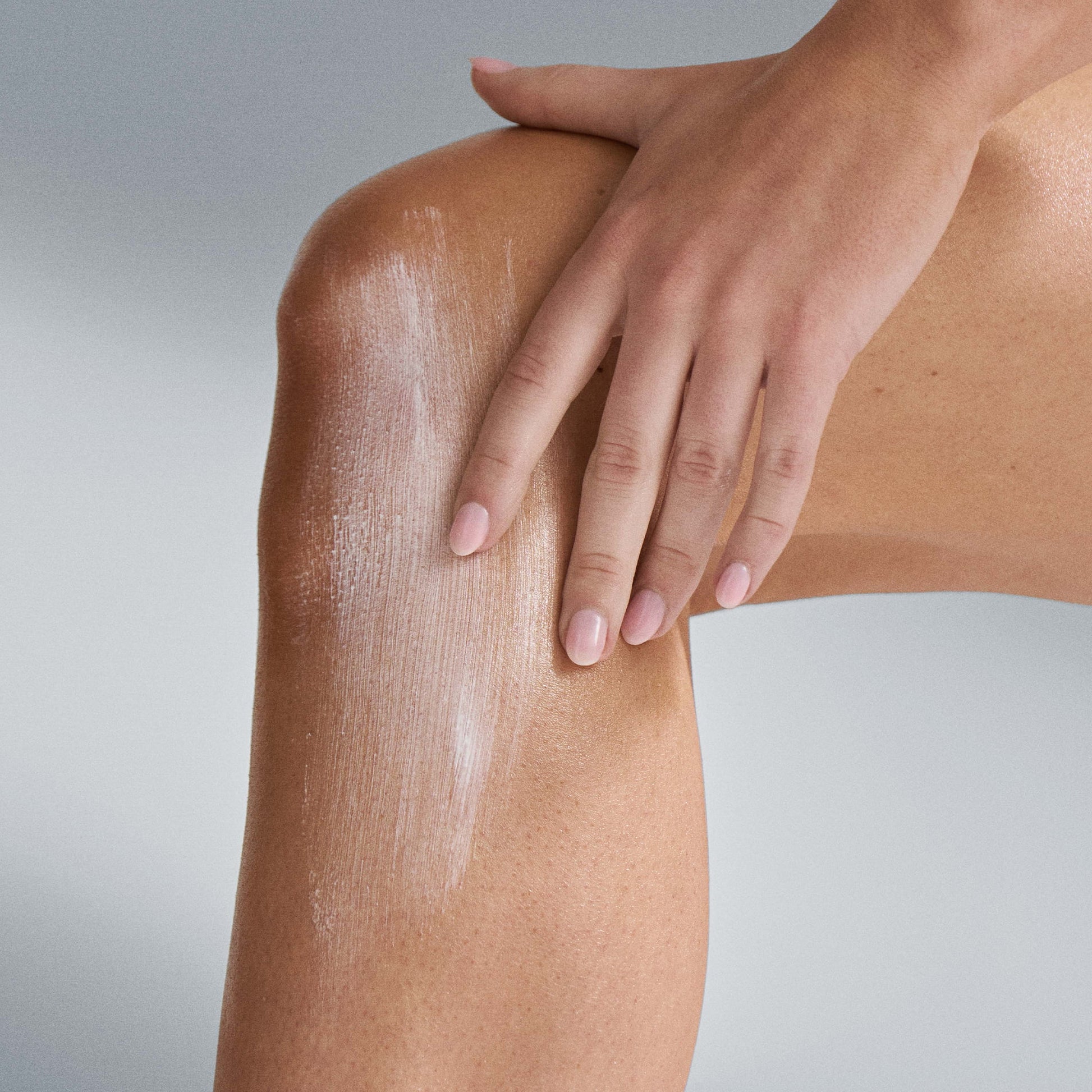 Black woman applying body sunscreen from a tube to her hand and forearm in warm daylight