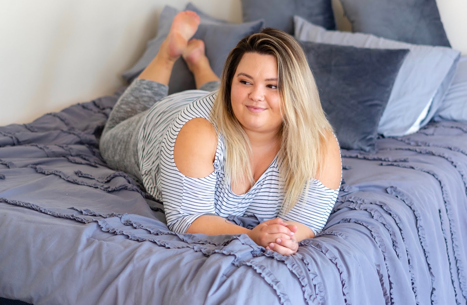 A plus-size woman sorting clothing into three piles on her bed during a closet purge, lit by warm lamplight