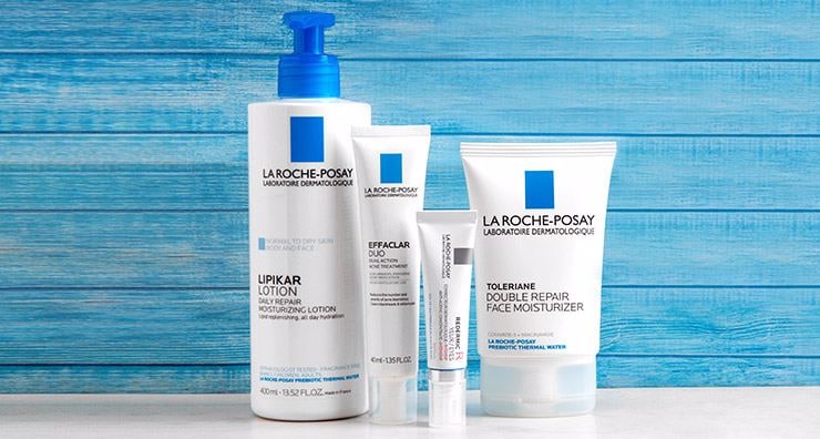 La Roche-Posay body care lineup on a marble vanity with a hand reaching for the Lipikar tube