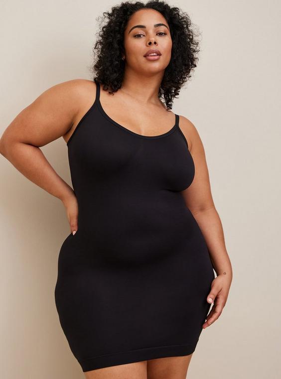 A plus-size woman smoothing a dress over shapewear, looking relaxed and confident