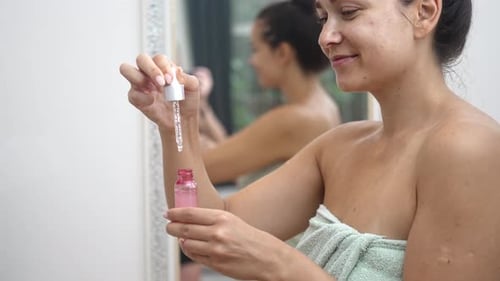 Woman applying affordable anti-aging serum in bathroom mirror