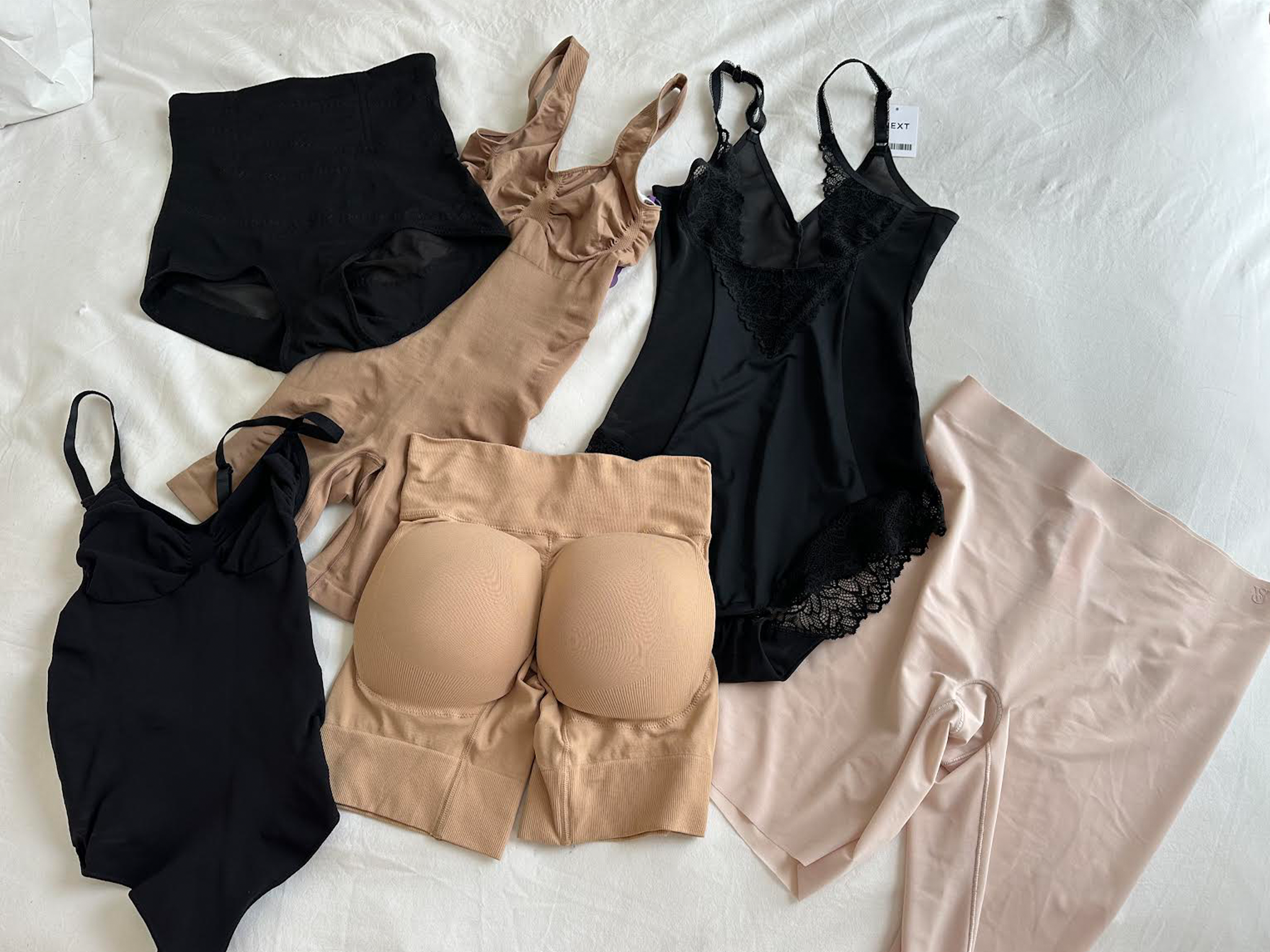 Assorted shapewear pieces in nude and black laid flat on a bed