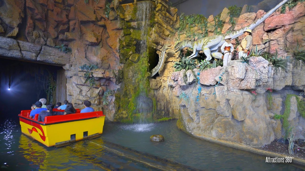 Boat ride vehicle with wide bench seating moving through a dark ride