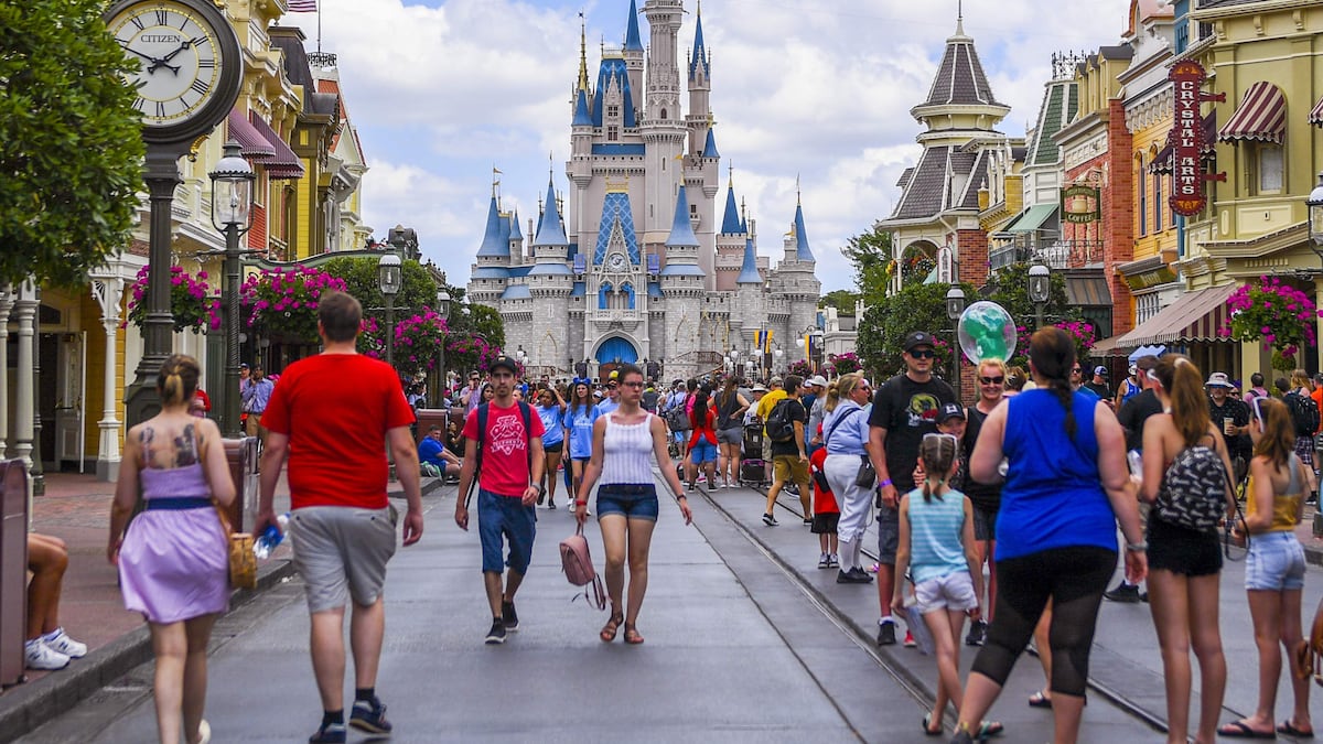 Theme park guests walking through a busy park entrance plaza in daylight